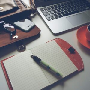 un pc portable sur un bureau avec une tasse de café, un agenda, un stylo, un sac à main ouvert